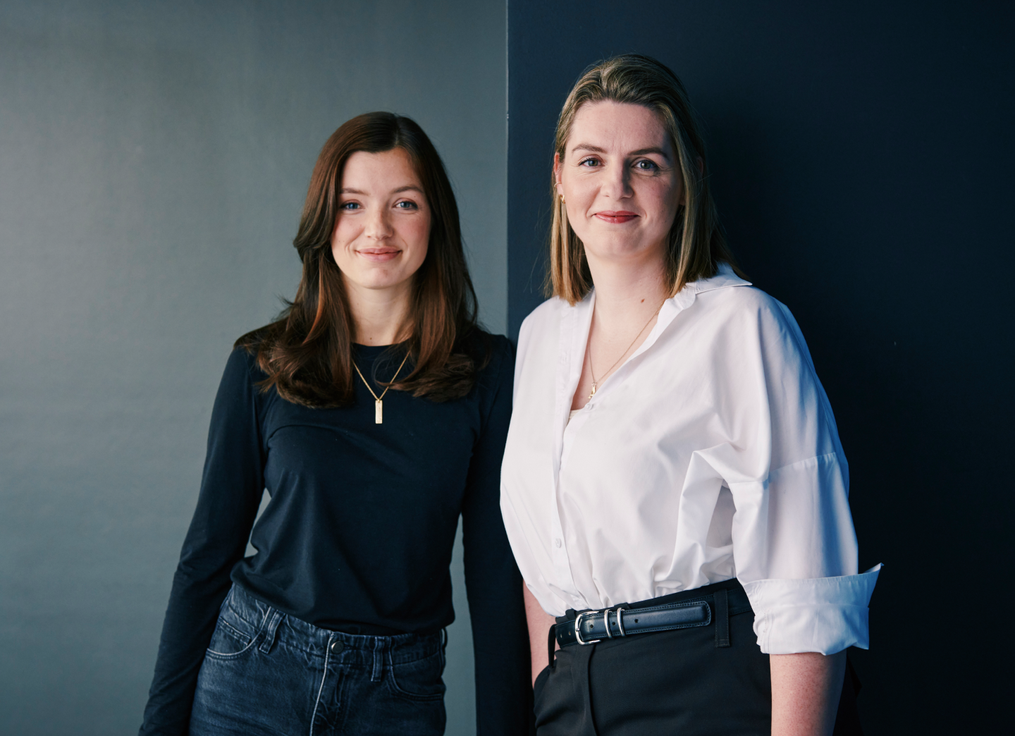 Lena Rogge und Anna Friesen, die neue Doppelspitze des Sparkassen Innovation Hubs, stehen nebeneinander vor einer dunklen Wand und lächeln in die Kamera.
