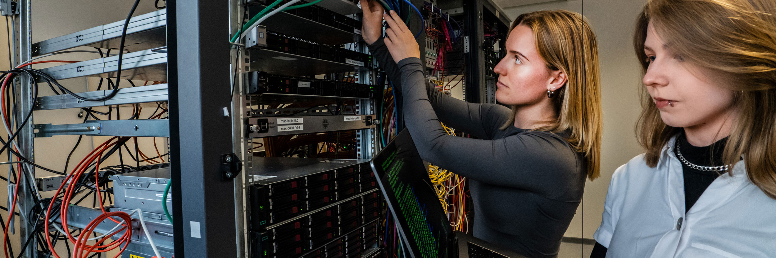 Zwei IT-Mitarbeiterinnen arbeiten im Serverraum an Kabeln und Netzwerktechnik – IT-Infrastruktur und Systemadministration bei Star Finanz.