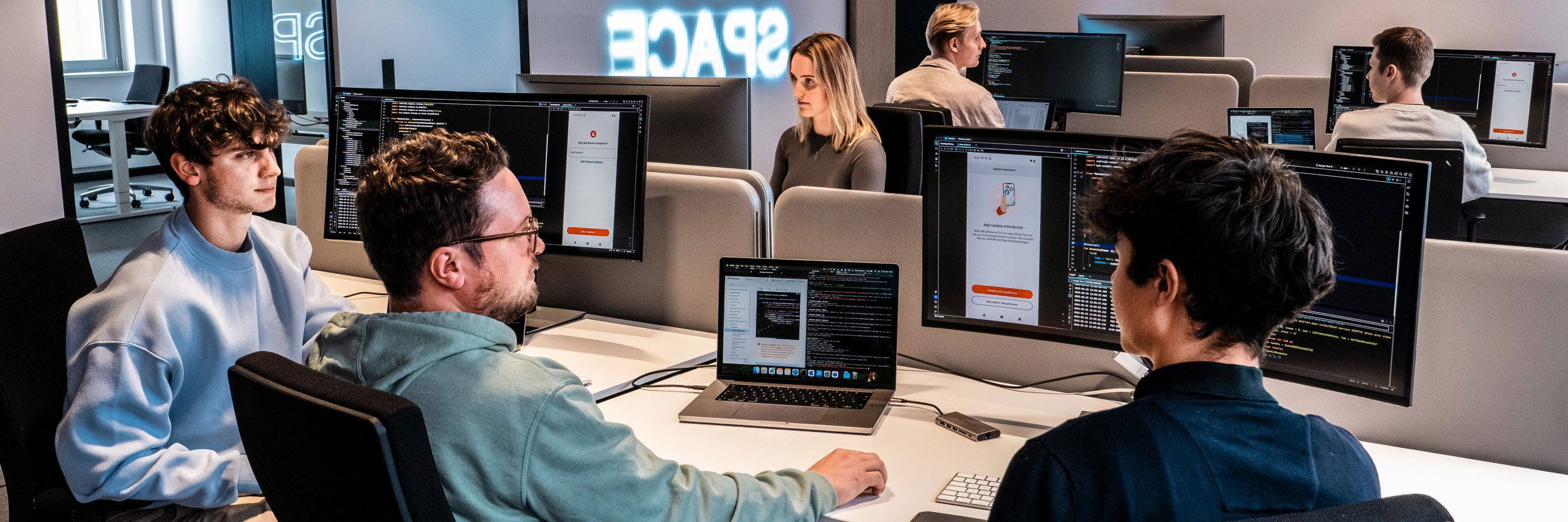 Softwareentwickler:innen der Star Finanz arbeiten im modernen Workspace mit mehreren Monitoren an der Programmierung und Gestaltung digitaler Anwendungen.