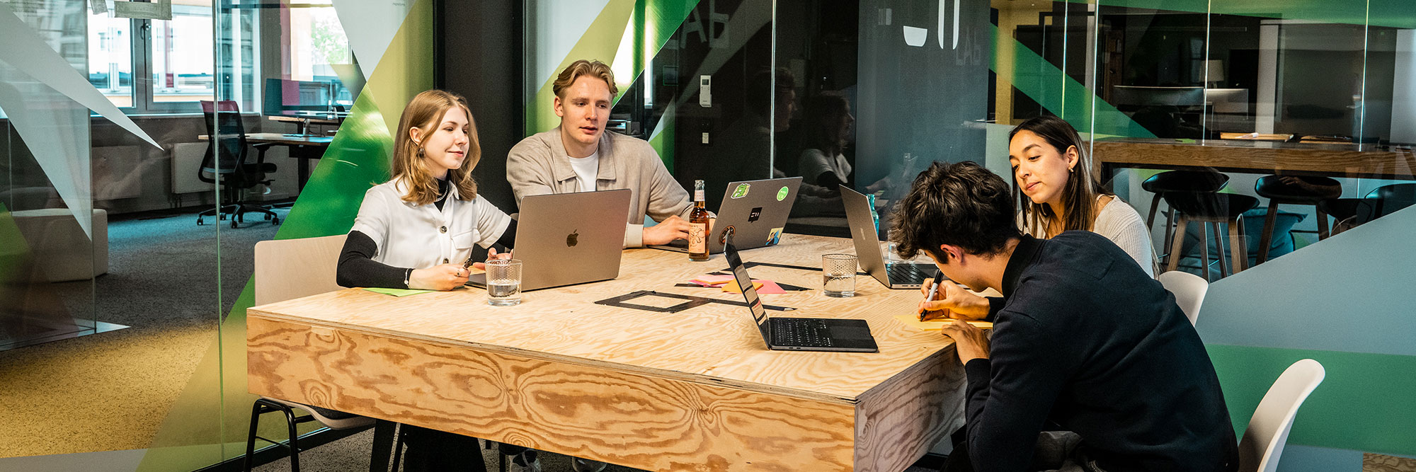 Vier Mitarbeiter:innen der Star Finanz arbeiten gemeinsam in einem modernen Meetingraum mit Laptops und Notizen – Teamwork und agile Zusammenarbeit.