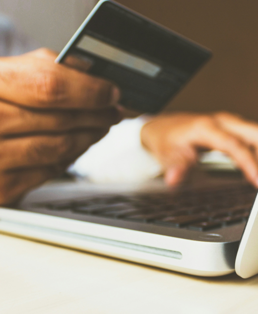 Person hält eine Kreditkarte in der Hand und gibt Daten auf einem Laptop ein – Symbolbild für Online-Zahlung und E-Commerce im Kontext Verification of Payee (VoP).