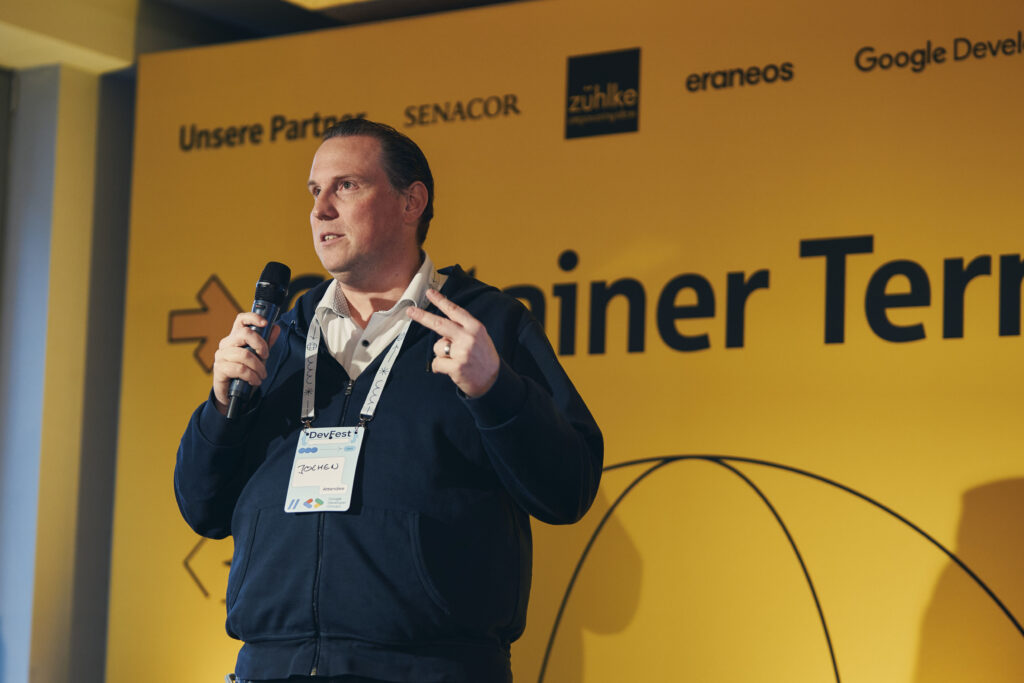 Jochen Balas begrüßt auf DevFest Hamburg 2025 mit einem Mikrofon das Publikum