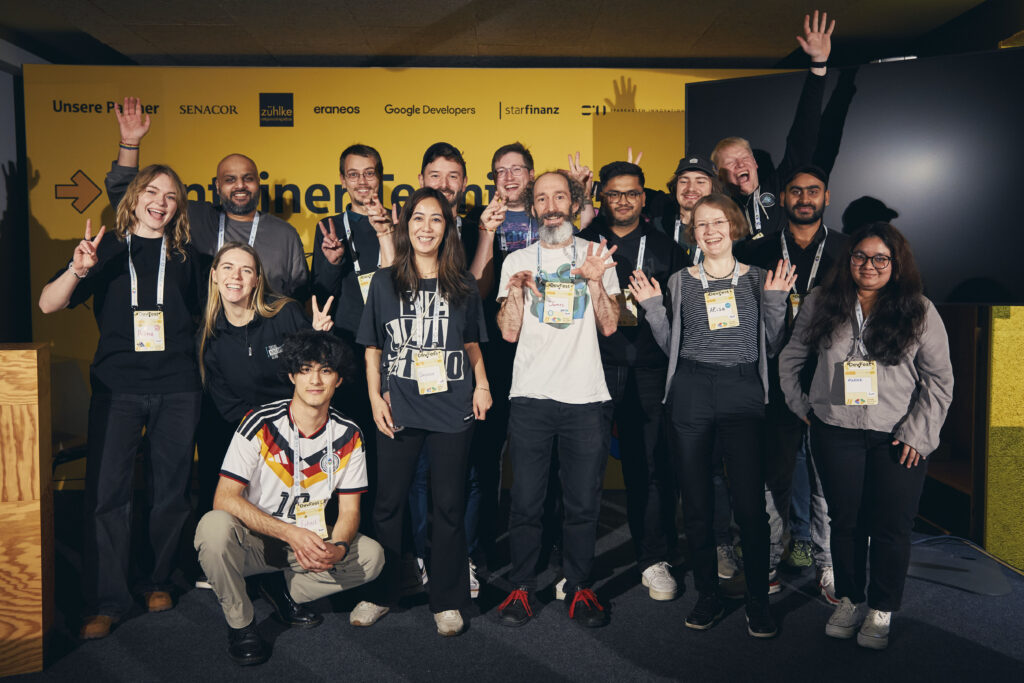 Das DevFest Orga-Team gesammelt abgebildet vor einer gelben Wand