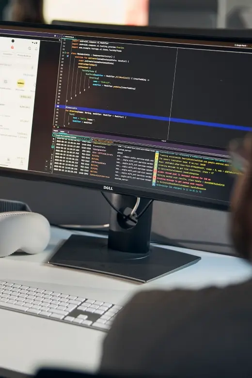 Ein großer Monitor auf einem Schreibtisch zeigt eine Entwicklungsumgebung mit Quellcode und Log-Ausgaben.