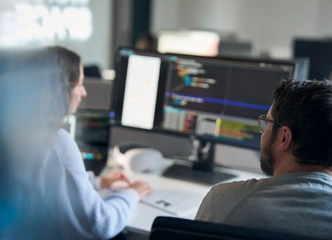 Zwei Star Finanz Mitarbeitende sitzen in einem Büro vor einem großen Bildschirm und schauen gemeinsam auf einen Code.