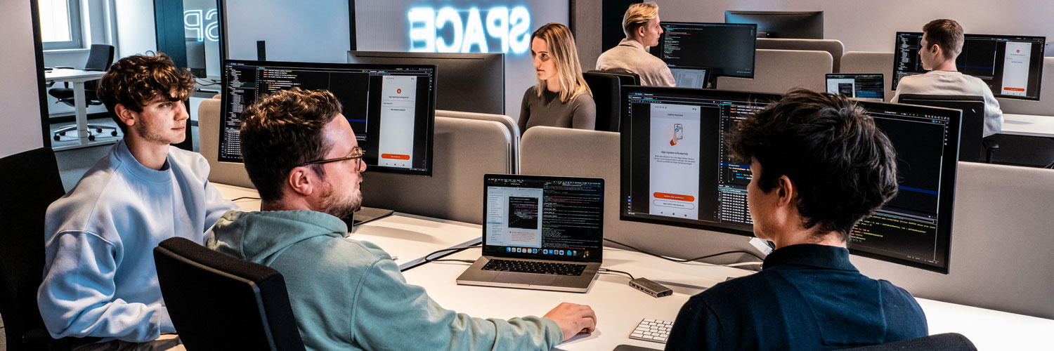 Duale Student:innen und Auszubildende sitzen zusammen und entwickeln Software.