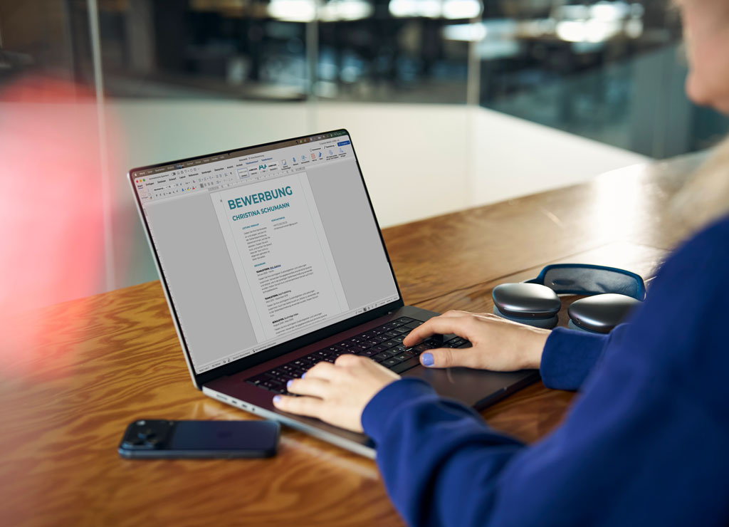 Eine Frau sitzt vor ihrem aufgeklappten Laptop und schreibt an ihrer Bewerbung.