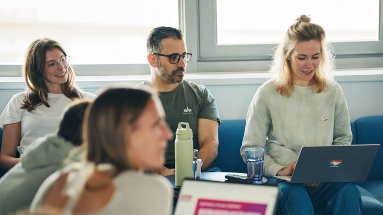 Vier Personen sitzen zusammen in einem Raum, drei von ihnen konzentrieren sich auf ihre Laptops.