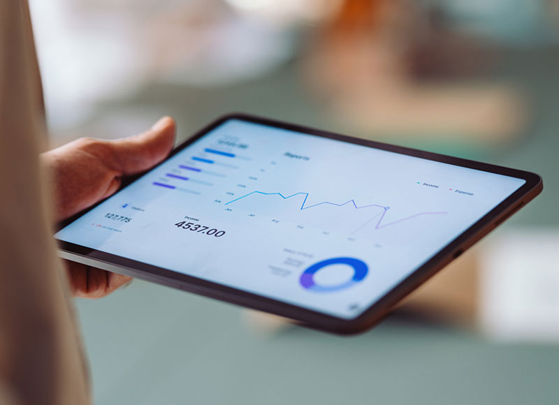 Blick auf ein in der Hand gehaltenes Tablet, auf dessen Screen Zahlen und der Jahresverlauf zu sehen sind.