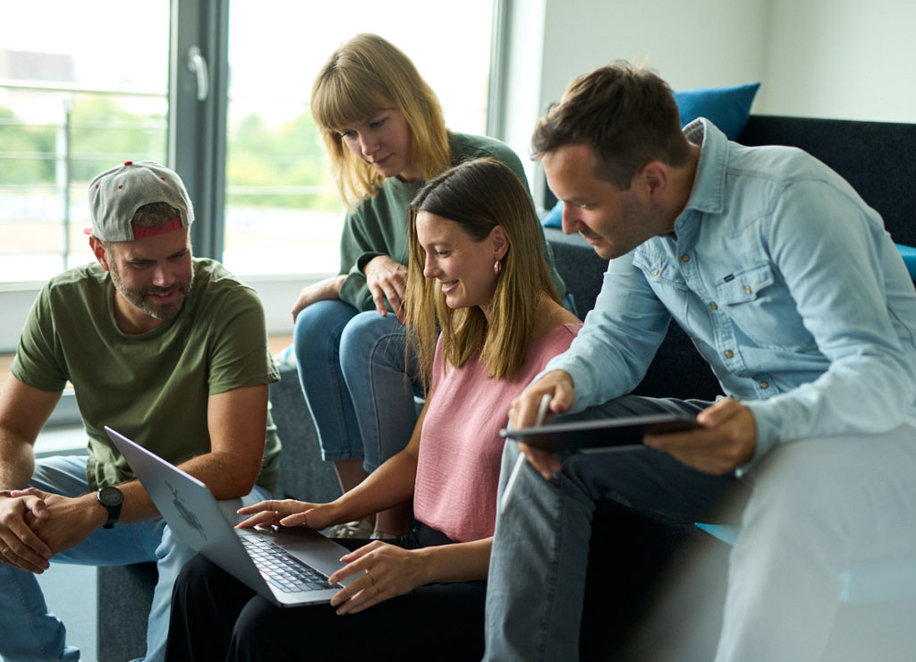 Vier Mitarbeiter sitzen und arbeiten zusammen und schauen gemeinsam auf ein Laptop.