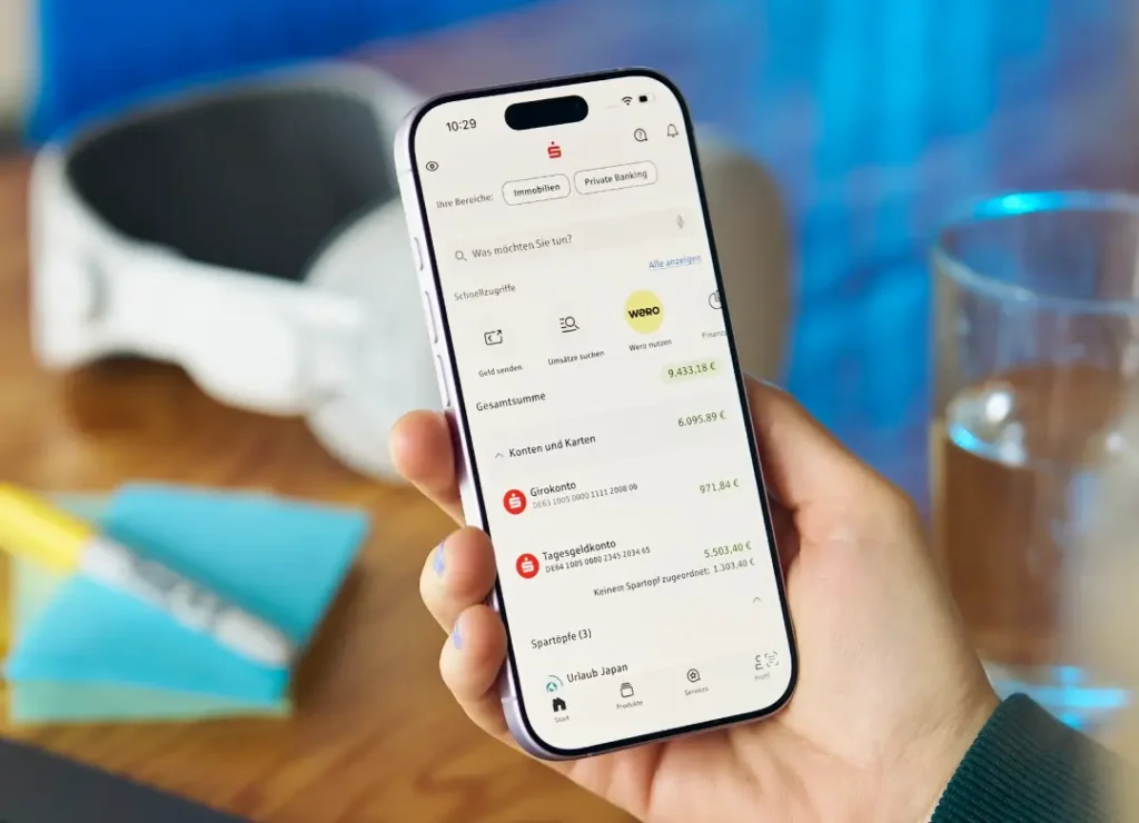 Eine Person hält ein Smartphone in der Hand, auf dessen Display die Sparkassen-App mit Kontenübersicht, Schnellzugriffen und aktuellen Kontoständen zu sehen ist.