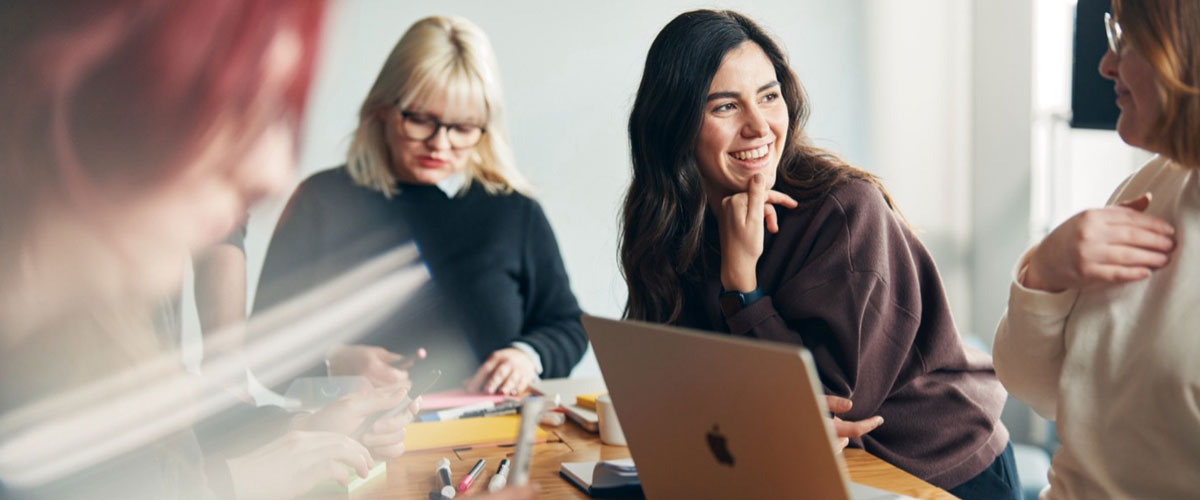 Vier junge Frauen arbeiten gemeinsam an einem Projekt an einem Tisch sitzen.