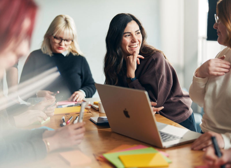 Vier junge Frauen arbeiten gemeinsam an einem Projekt an einem Tisch sitzen.