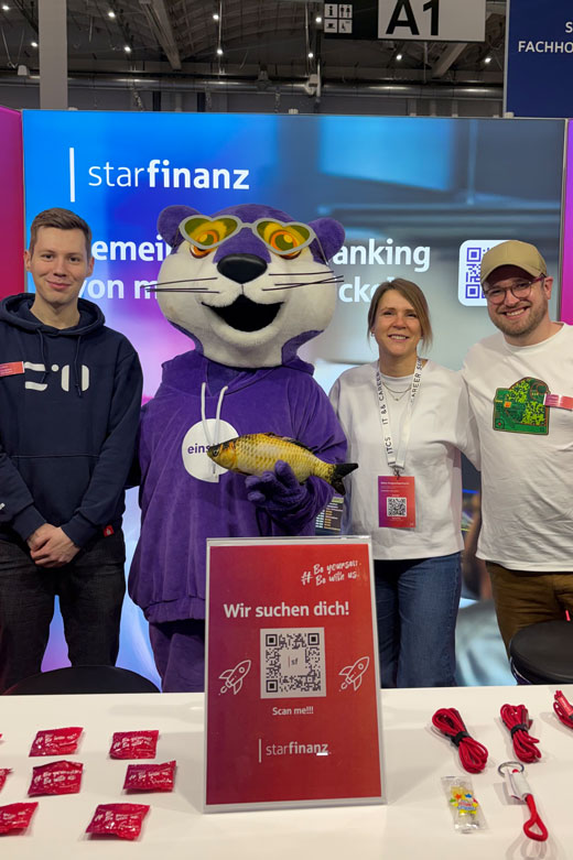 Zwei Mitarbeiter und eine Mitarbeiterin der Star Finanaz stehen mit einem lebnsgroßen Maskottchen auf dem Messestand einer Personalmesse.