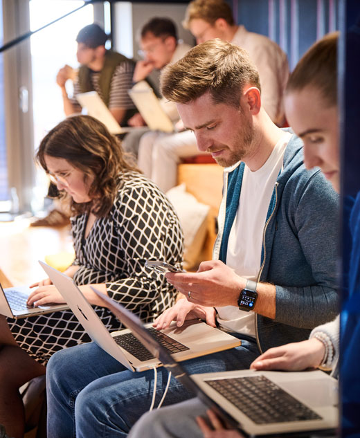 Diverse Personen sitzen auf einer Tribüne im Rahmen eines Workshops und arbeiten an ihren Rechnern.