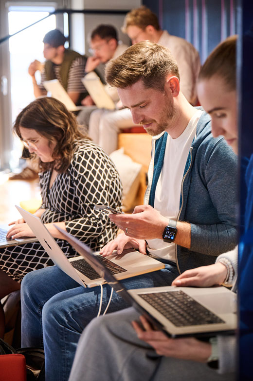 Diverse Personen sitzen auf einer Tribüne im Rahmen eines Workshops und arbeiten an ihren Rechnern.