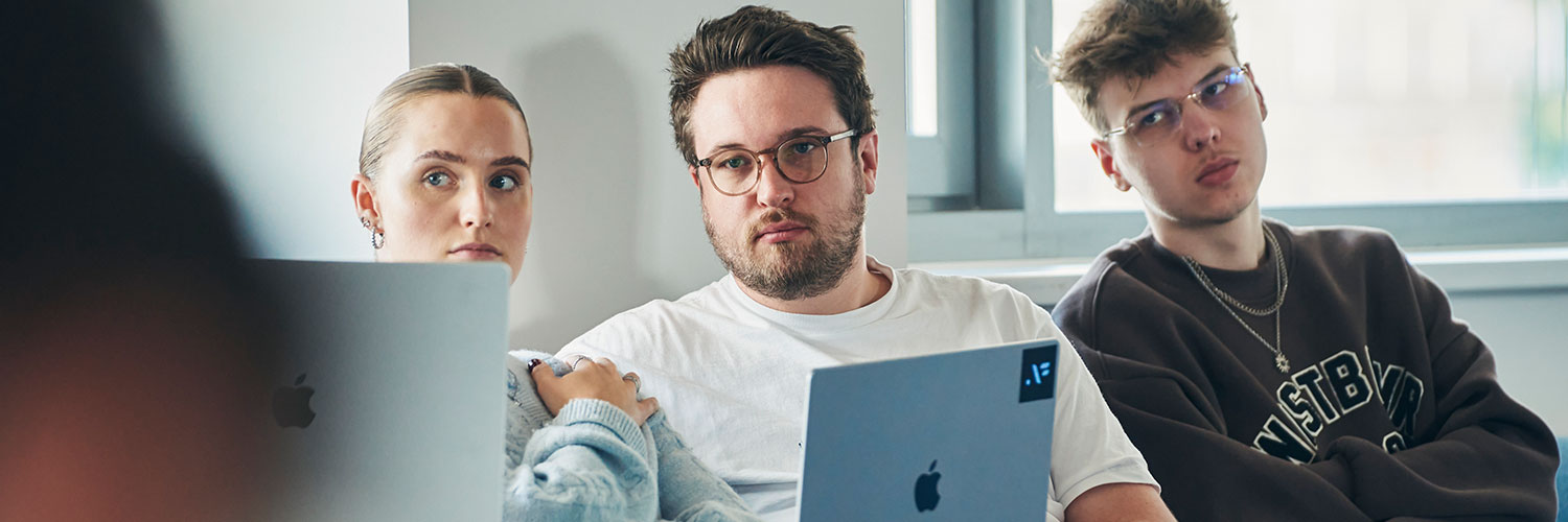 Drei junge Mitarbeitende sitzen gemeinsam in einem Workshop und hören einem Vortrag zu.