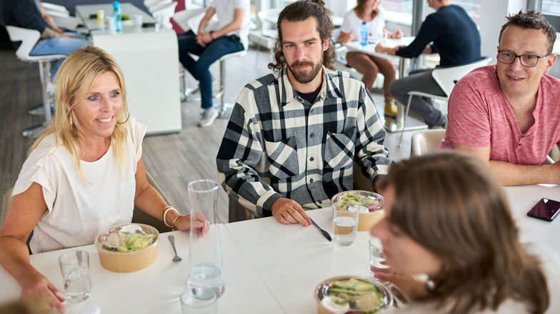 Ein Mann und seine Kolleg:innen sitzen zusammen zum Mittagessen in der Kantine.