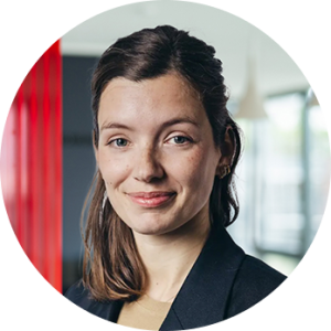 Porträtfoto von Lena Rogge, Co-Leiterin des Sparkassen Innovation Hubs, Frau mit braunen Haaren, die seitlich zurückgesteckt sind. Sie trägt einen schwarzen Blazer und lächelt leicht. Der Hintergrund zeigt ein modernes Büro mit roten und grauen Elementen.