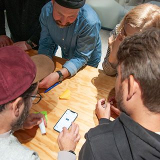 Vier Kolleg:innen beugen sich über ein Smartphone und verproben eine neu entwickelte App.