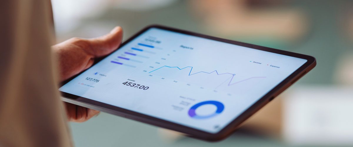 Blick auf ein in der Hand gehaltenes Tablet, auf dessen Screen Zahlen und der Jahresverlauf zu sehen sind.