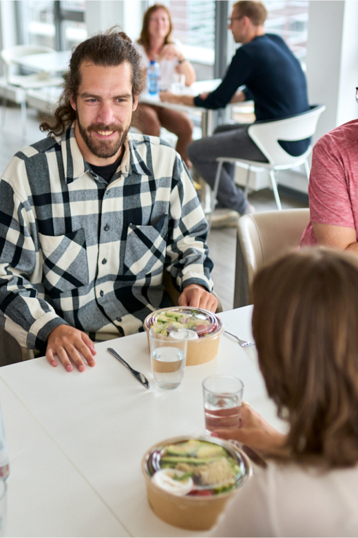 Ein Mann und seine Kolleg:innen sitzen zusammen zum Mittagessen in der Kantine.