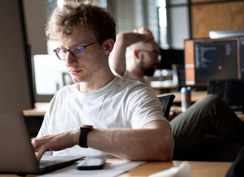 Junger Mann sitzt am Rechner und programmiert.