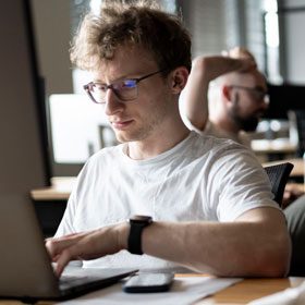 Junger Mann sitzt am Rechner und programmiert.