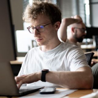 Junger Mann sitzt am Rechner und programmiert.