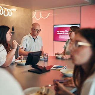 Fünf Kolleg:innen sitzen zusammen beim Mittagessen.