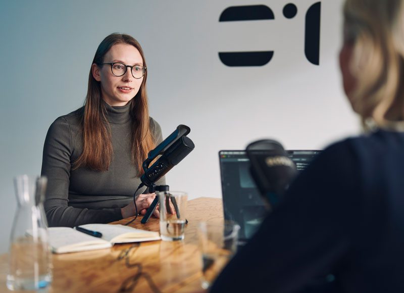 Eine Frau sitzt einer zweiten Person in einem Podcast Studio gegenüber.