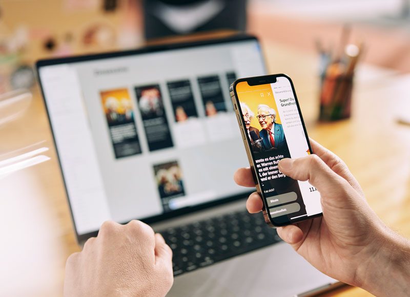 Es wird ein Prototyp auf dem Smartphone gezeigt und im Hintergrund ist ein aufgeklappter Laptop zu sehen.