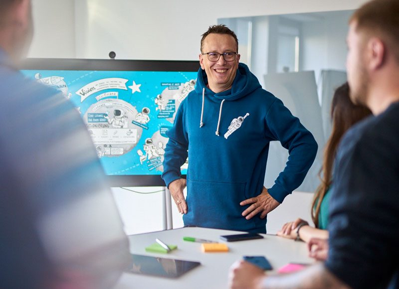 Ein Mann steht vor einem Screen und erklärt den Kolleg:innen die Unternehmensvision.