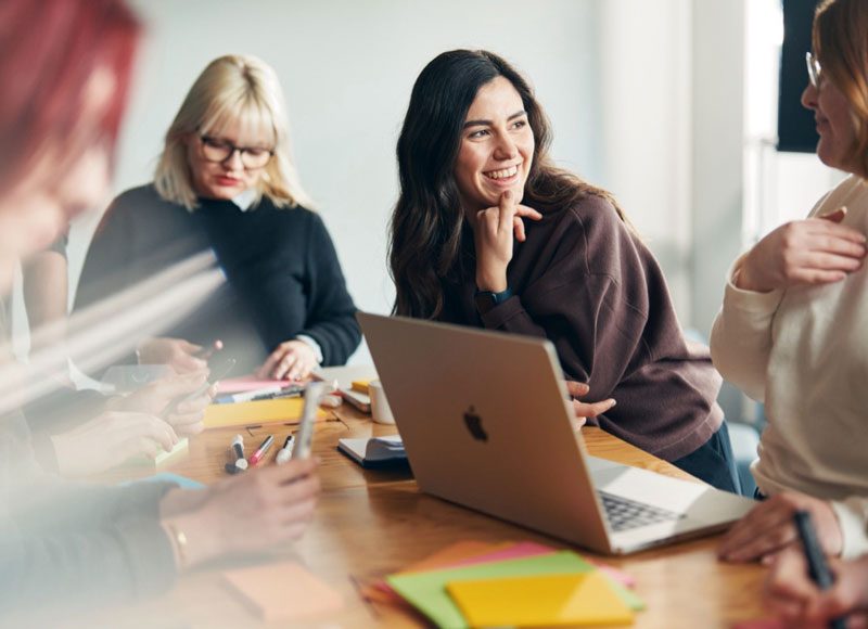 Vier junge Frauen arbeiten gemeinsam an einem Projekt an einem Tisch sitzen.
