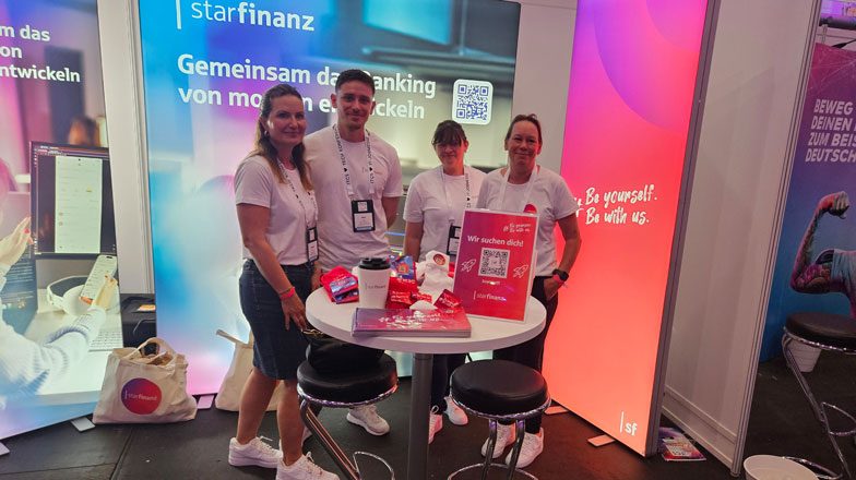 Ein Mitarbeiter und drei Mitarbeiterinnen der Star Finanaz stehend fröhlich lachend vor dem Messestand bei der Personalmesse ITCS.