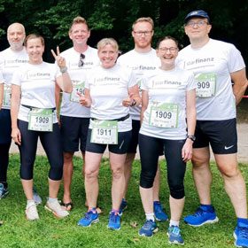 Sieben Personen in einheitlichen weißen Hemden und Laufbekleidung stehen im Freien, lächeln und posieren gemeinsam für ein Gruppenfoto; jede von ihnen trägt eine Startnummer.