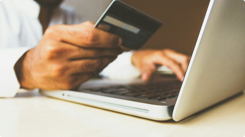 Person hält eine Kreditkarte in der Hand und gibt Daten auf einem Laptop ein – Symbolbild für Online-Zahlung und E-Commerce im Kontext Verification of Payee (VoP).